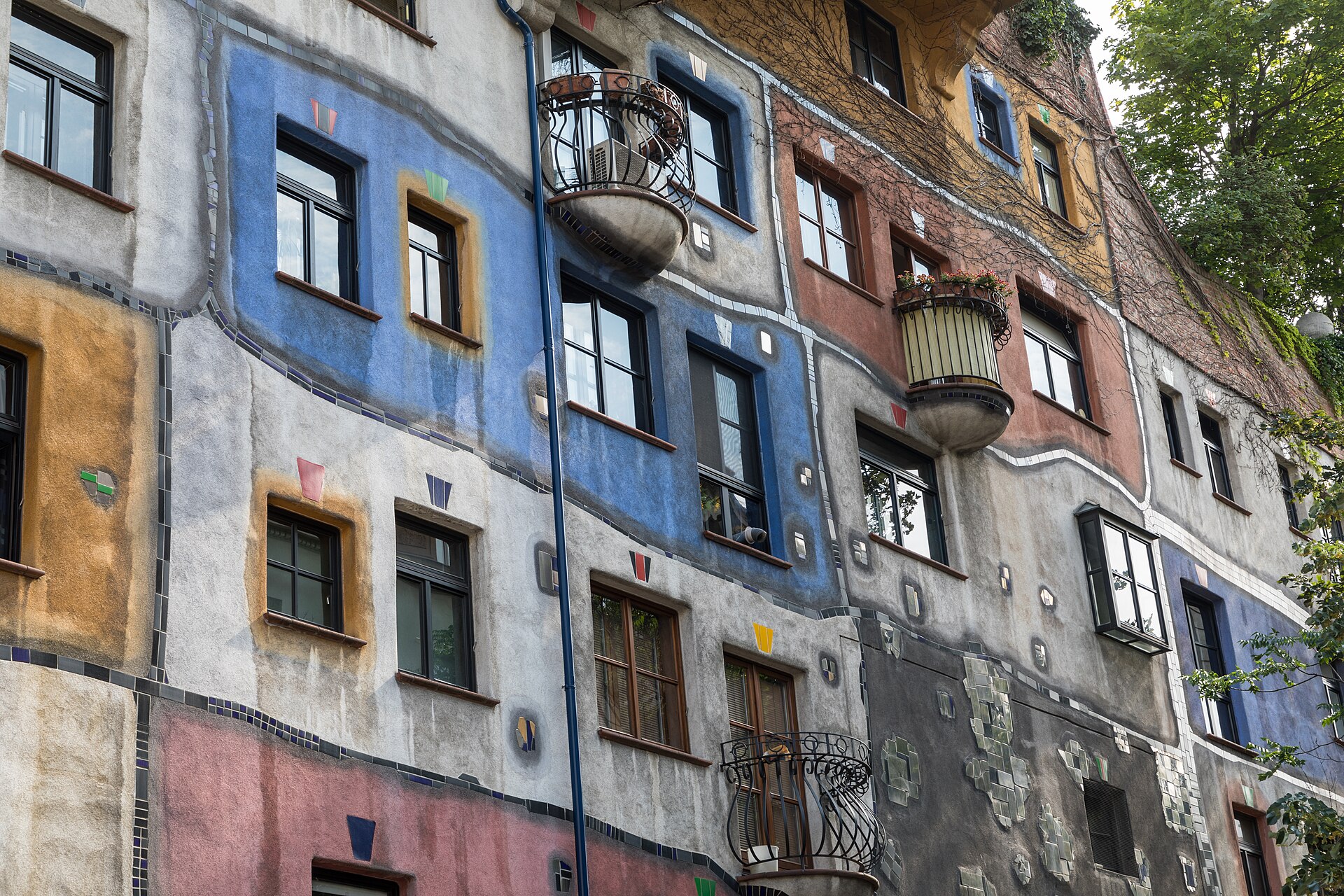 Facade of the Hundertwasserhaus in Vienna: irregular colour fields, uneven window placement, ceramic columns and planted terraces.