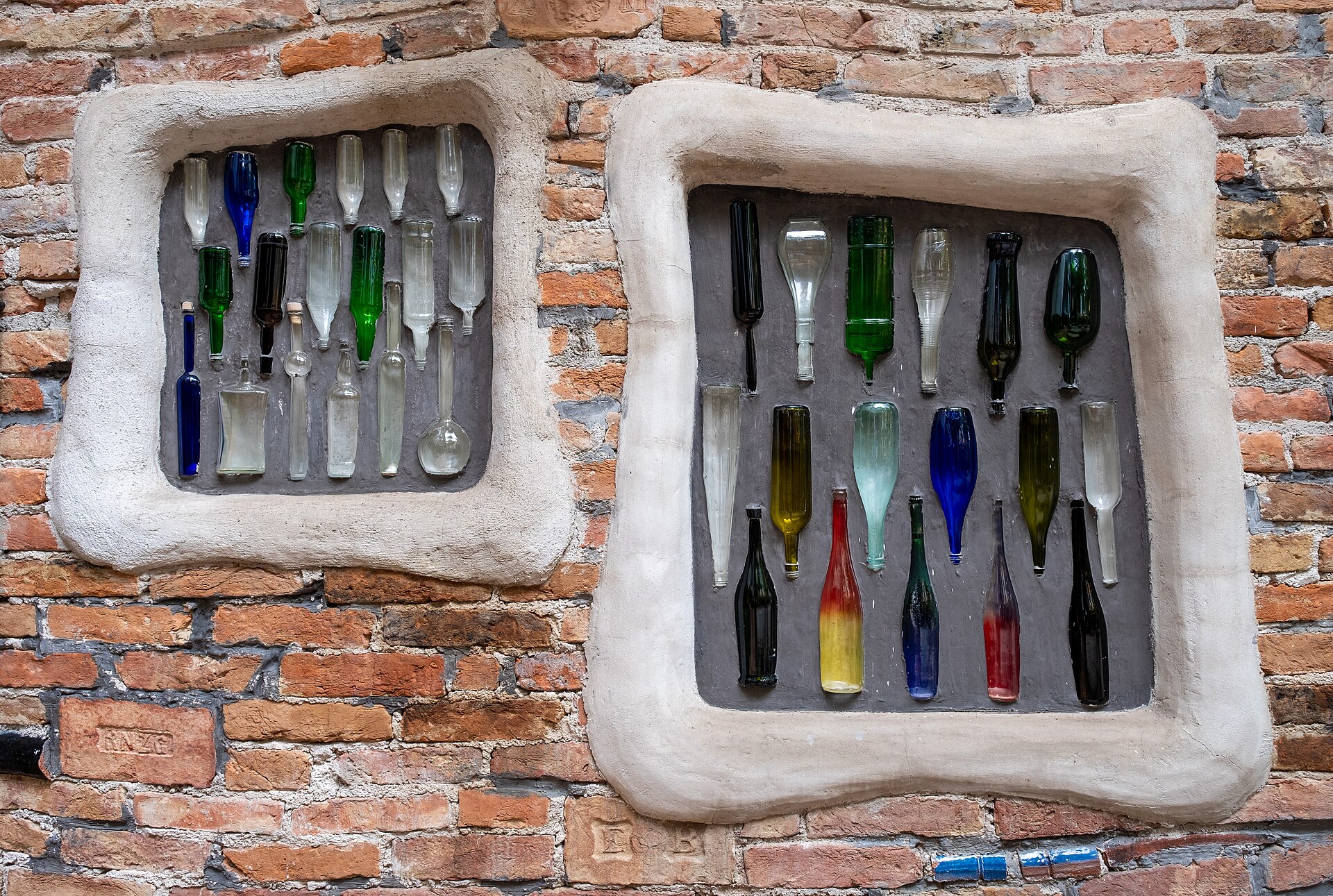 Courtyard wall at KunstHausWien: glass bottles set into wavy hand-formed plaster frames on brick.