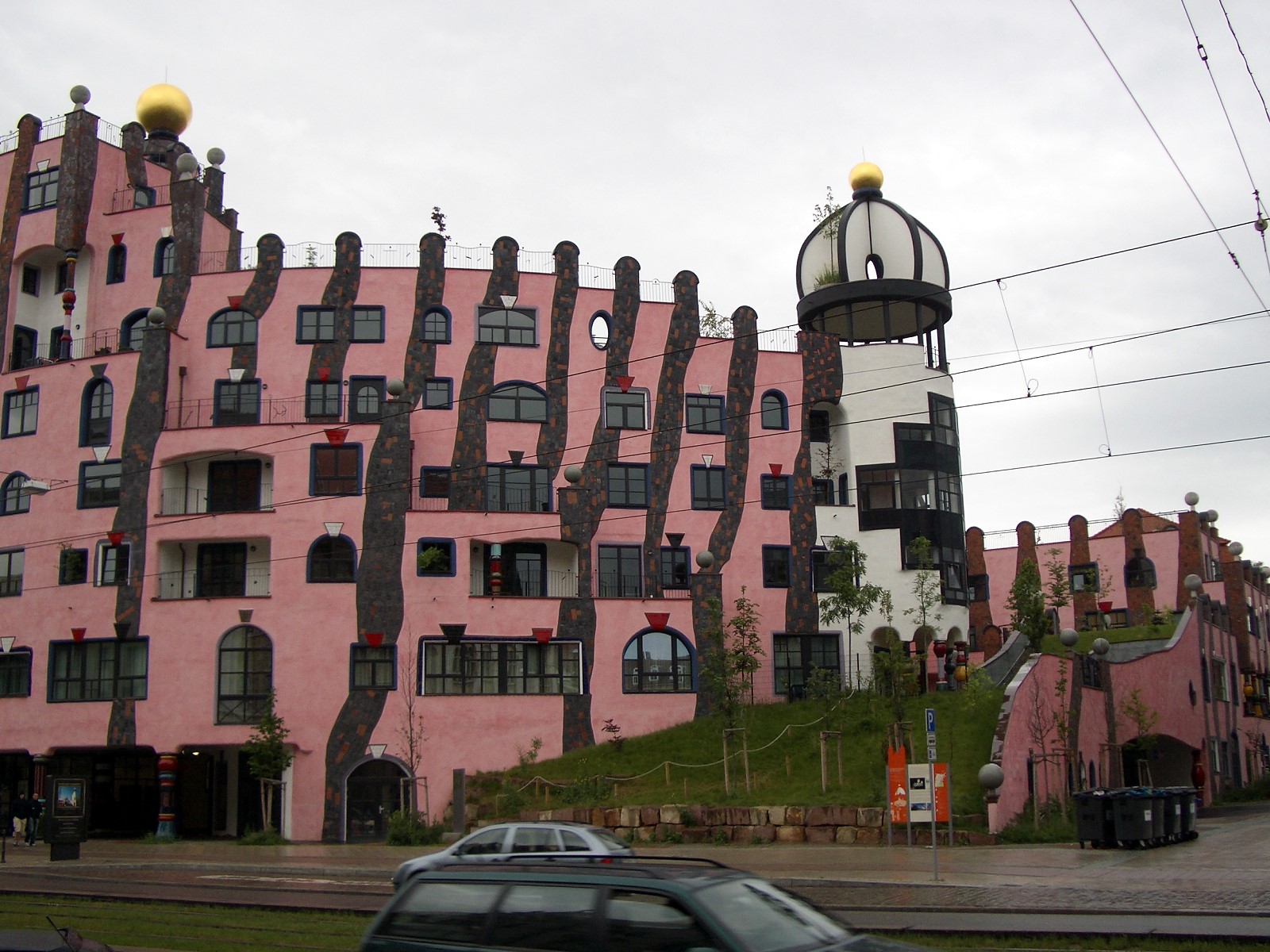 The Grüne Zitadelle in Magdeburg: a rose-pink building with irregular windows and mature trees growing from its roof.